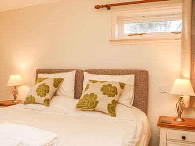A bedroom with a double bed two lamps on bedside tables and a small window at Fig Tree Cottage in Bickleigh