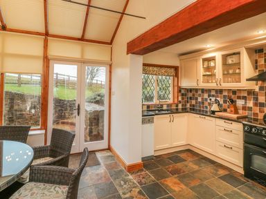 A kitchen with tiled floor and walls with white cabinets and black countertops at Fig Tree Cottage in Bickleigh