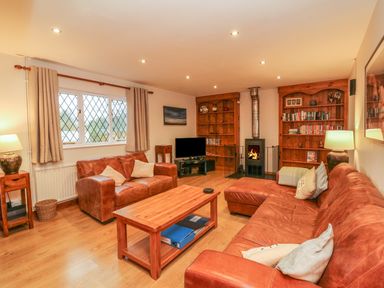 A living room with leather sofas a wooden coffee table bookshelves and a fireplace at Fig Tree Cottage in Bickleigh