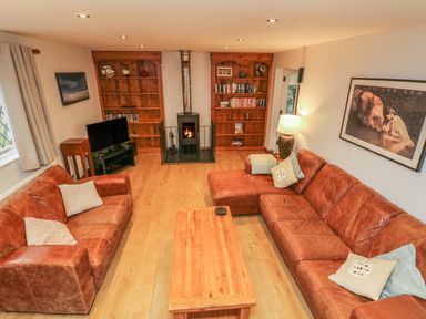 A living room with two brown leather sofas a wooden coffee table bookshelves and a fireplace at Fig Tree Cottage in Bickleigh