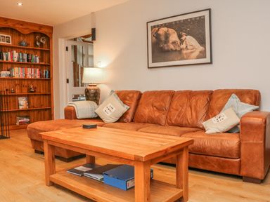 A living room with a brown leather sofa wooden coffee table and bookshelf at Fig Tree Cottage in Bickleigh