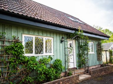 A green wooden house with diamond pane windows and climbing plants at Fig Tree Cottage in Bickleigh