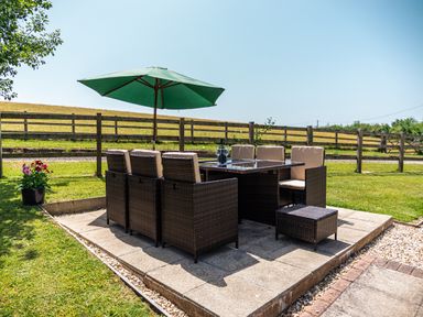An outdoor patio area with a dining table and chairs under a green umbrella at Fig Tree Cottage in Bickleigh