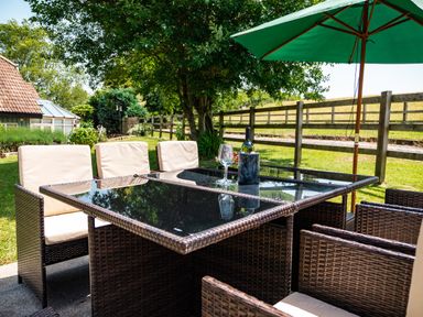 Outdoor patio table with chairs and a green umbrella in a garden setting at Fig Tree Cottage in Bickleigh