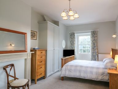 A bedroom with a double bed wooden furniture a window with patterned curtains and a ceiling light at Tick Tock Cottage in Marnhull