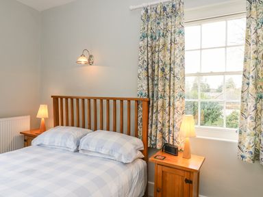 A bedroom with a double bed flanked by wooden nightstands with lamps and floral curtains at Tick Tock Cottage in Marnhull