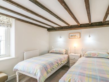 A bedroom with two single beds a nightstand and exposed wooden ceiling beams at Tick Tock Cottage in Marnhull