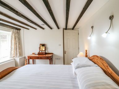 A bedroom with a wooden bed white pillows a wooden dressing table with a mirror and a window with curtains at Tick Tock Cottage in Marnhull