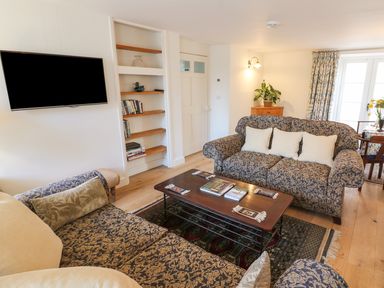 A living room with patterned sofas a wooden coffee table bookshelves and a wall-mounted TV at Tick Tock Cottage in Marnhull
