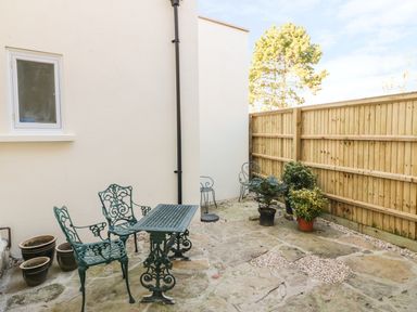 An outdoor patio area with metal table and chairs potted plants and a wooden fence at Tick Tock Cottage in Marnhull