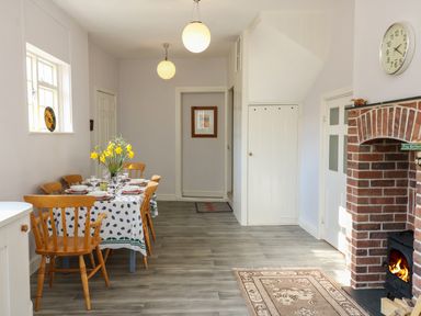 A dining area with a table set for six people and a brick fireplace with a wood stove at Tick Tock Cottage in Marnhull