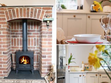 A brick fireplace with a wood burning stove firewood and kitchen cabinets with a table setting at Tick Tock Cottage in Marnhull