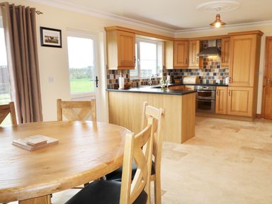 A kitchen with wooden cabinets round wooden dining table and chairs near a door and window at Benbulben View in Tullaghan County Leitrim