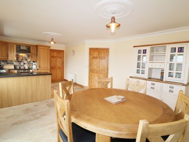 A kitchen and dining area with a round wooden table and chairs a white cabinet and wooden kitchen cabinets at Benbulben View in Tullaghan County Leitrim