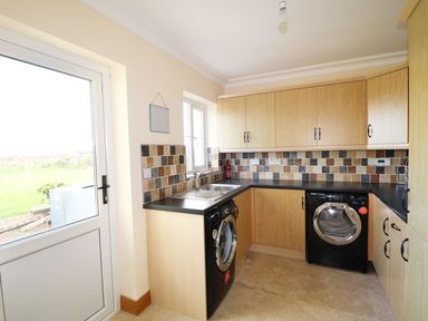 A utility room with wooden cabinets black countertop washing machine and dryer at Benbulben View in Tullaghan County Leitrim