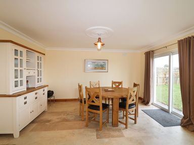 A dining room with a round wooden table and six chairs next to glass sliding doors and a white cabinet at Benbulben View in Tullaghan County Leitrim