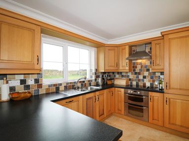 A kitchen with wooden cabinets black countertops a stainless steel oven and a window overlooking a stone wall at Benbulben View in Tullaghan County Leitrim