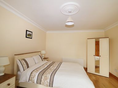 A bedroom with a bed with patterned bedding two bedside tables with lamps a wardrobe with mirrored door and a framed picture on the wall at Benbulben View in Tullaghan County Leitrim