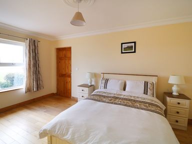 A bedroom with a bed two bedside tables with lamps a window with curtains and a wooden door at Benbulben View in Tullaghan County Leitrim