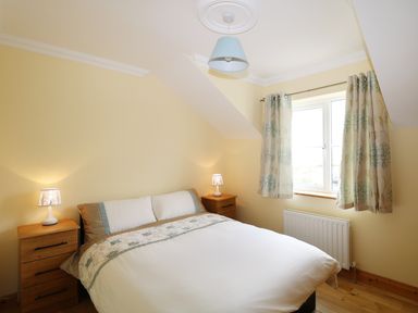 A bedroom with a bed white and floral bedspread wooden side tables with lamps and floral curtains at Benbulben View in Tullaghan County Leitrim