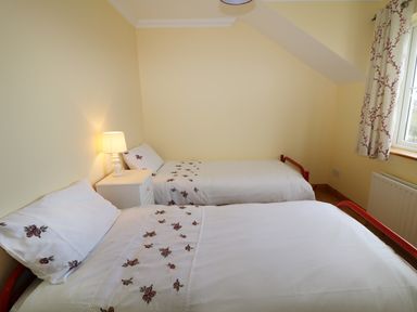 A bedroom with two single beds a nightstand with a lamp and a window with floral curtains at Benbulben View in Tullaghan County Leitrim