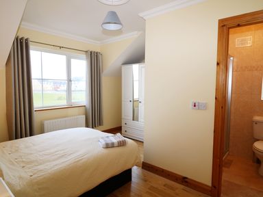 A bedroom with a bed and folded towels on it a window with curtains a white wardrobe and an open door leading to a bathroom at Benbulben View in Tullaghan County Leitrim