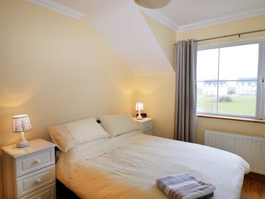 A bedroom with a double bed, two bedside tables with lamps, a window with curtains, and a folded towel on the bed at Benbulben View in Tullaghan County Leitrim