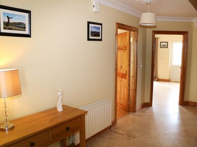 A hallway with a wooden console table with a lamp and sculpture two framed pictures on the wall and wooden doors at Benbulben View in Tullaghan County Leitrim