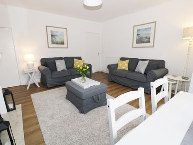A living room with two gray sofas a gray ottoman with flowers on it a white rug and white dining chairs at Rose Cottage in Lesbury near Alnmouth