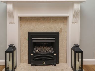 A fireplace with black metal grate and stones inside flanked by two black lanterns with candles at Rose Cottage Lesbury near Alnmouth