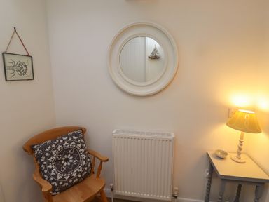 A wooden chair with a patterned cushion next to a radiator and a small table with a lamp and bowl at Rose Cottage in Lesbury near Alnmouth