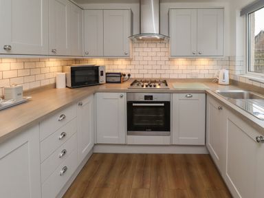 A kitchen with white cabinets a built in oven microwave kettle and a sink at Rose Cottage Lesbury near Alnmouth