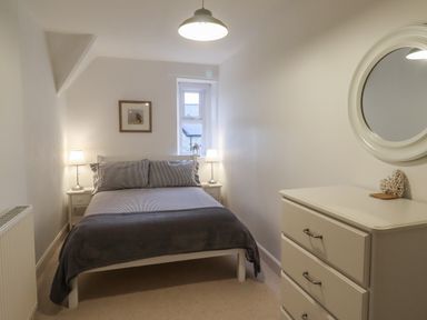A bedroom with a double bed bedside tables with lamps a chest of drawers with a mirror and a small window at Rose Cottage in Lesbury near Alnmouth