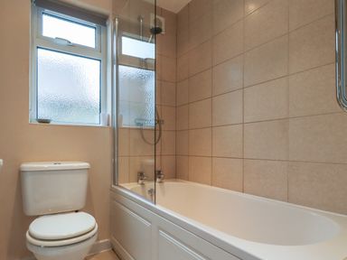 A bathroom with a toilet and a bathtub with tiled walls and a frosted window at Rose Cottage in Lesbury near Alnmouth