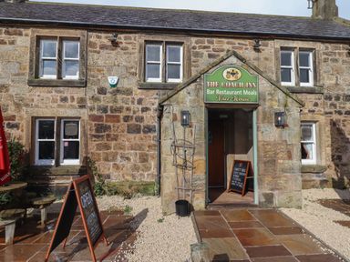 The stone exterior of The Coach Inn with a sign above the entrance and sandwich boards outside