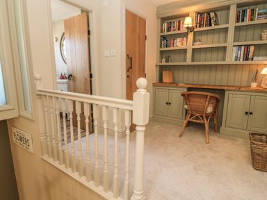 A small home office area with built in shelves and cabinets a wicker chair and a carpeted floor at The Olde Stables in Warkworth