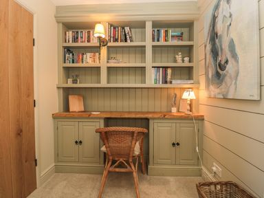 A study area with built-in shelves filled with books a wooden desk chair and a horse painting on the wall at The Olde Stables in Warkworth