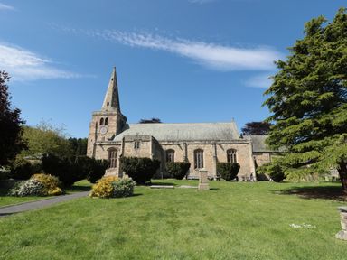 A stone church with a clock tower surrounded by grass and trees at The Olde Stables in Warkworth