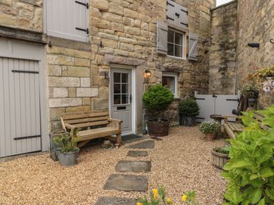An outdoor courtyard with stone walls wooden benches potted plants and a gravel walkway at The Olde Stables in Warkworth