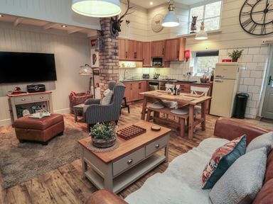 An open plan living room and kitchen with wooden furniture and a wall mounted television at The Olde Stables in Warkworth