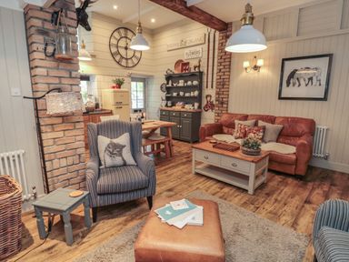 A living room with a leather sofa striped armchairs a coffee table and kitchen area at The Olde Stables in Warkworth