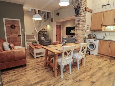 An open plan living area with a dining table and chairs a sofa armchairs stairs washing machine and kitchen cabinets at The Olde Stables in Warkworth