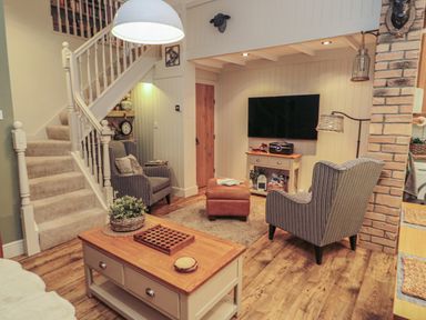 A living room with two striped armchairs a brown ottoman a wooden coffee table and a mounted television at The Olde Stables in Warkworth