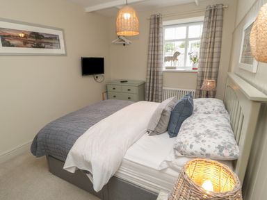A bedroom with a bed pillows and comforter a dresser and a window with curtains at The Olde Stables in Warkworth
