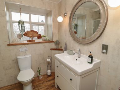 A bathroom with a toilet white sink with drawers round mirror and wooden fish decoration at The Olde Stables in Warkworth