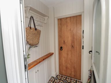 An entryway with a wooden door white cabinets a straw bag hanging on hooks and patterned tile flooring at The Olde Stables in Warkworth