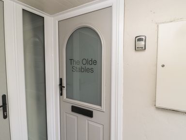 A door with frosted glass and the text The Olde Stables on it next to a wall with a master lock at The Olde Stables in Warkworth