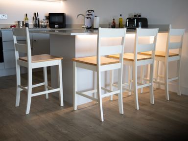 A kitchen island with four white bar stools with wooden seats at Chapel Rock View The Dunes in Perranporth