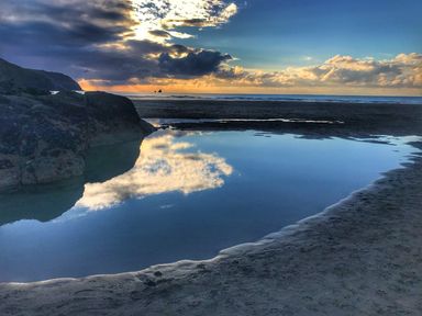 A beach with water puddle reflecting clouds and rocks at Chapel Rock View The Dunes in Perranporth
