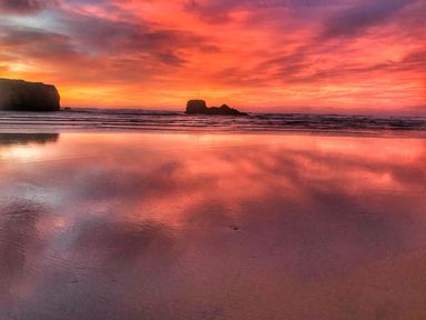 A beach with rock formations and a colorful sunset sky reflecting on wet sand at Chapel Rock View The Dunes in Perranporth